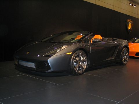 1993 Ford Taurus - Dark grey Lamborghini Gallardo Spyder on display with an orange car in the background.