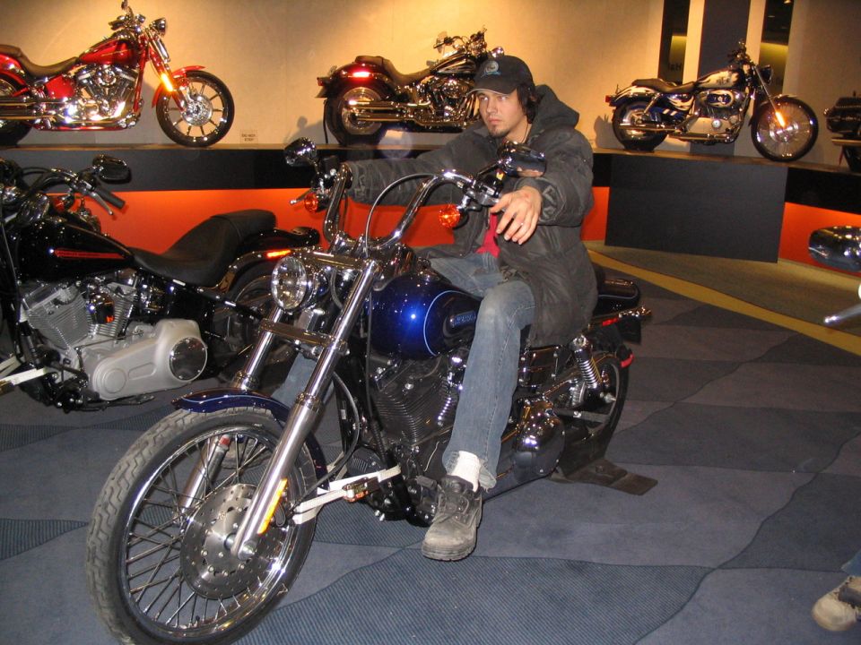 Man sits on a blue motorcycle with chrome accents. Other motorcycles are displayed in the background