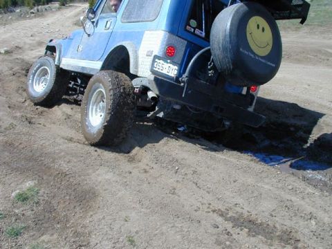 1979 Ford Bronco - Off-road SUV navigates a dirt track, spare tire mounted on the rear.