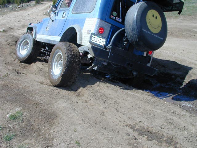 Blue off-road SUV with spare tire on back, driving on dirt. License plate 355-DYO