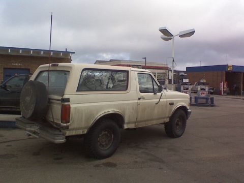 1992 Ford Bronco - A dirty white 1992 Ford Bronco is parked at a gas station under a cloudy sky.