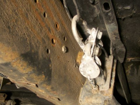 1995 Ford C-350 (Centurion Conversions) - Underside view of a vehicle's rusty frame, showing a metal bracket and chain assembly.