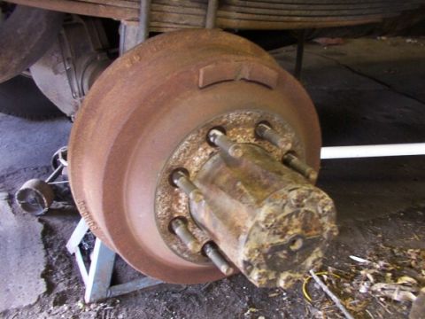 1995 Ford C-350 (Centurion Conversions) - A close-up view of a heavily rusted brake rotor and hub assembly, supported by jack stands.