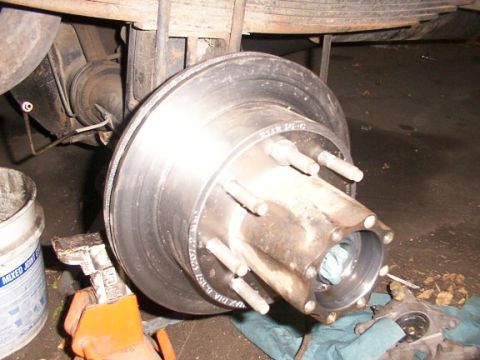 1995 Ford C-350 (Centurion Conversions) - Close-up of a vehicle's rear brake rotor and hub assembly, supported by a jack stand.