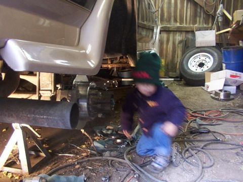 1995 Ford C-350 (Centurion Conversions) - A child is seen in a garage, working on the undercarriage of a vehicle.