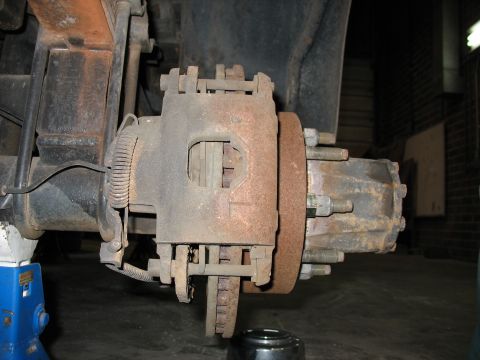 1995 Ford C-350 (Centurion Conversions) - Rusty brake caliper and rotor assembly on a truck, supported by a blue jack stand.