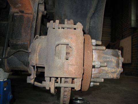 1995 Ford C-350 (Centurion Conversions) - Close-up of a heavily rusted truck brake caliper, rotor, and hub assembly.