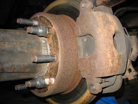 1995 Ford C-350 (Centurion Conversions) - Close-up view of a heavily rusted brake caliper and rotor assembly on a vehicle's axle.