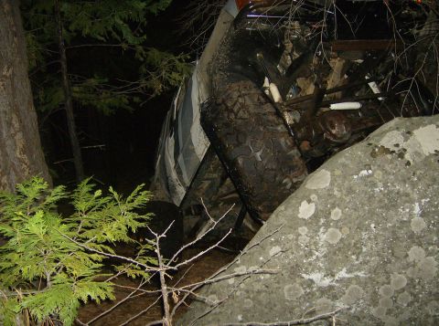 1986 Ford Bronco - Vehicle appears to be stuck off-road, wedged between large rocks and trees.