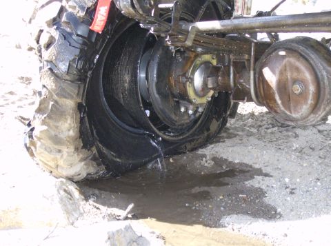 1986 Ford Bronco - The rear axle and a flat tire are shown with fluid leaking onto the ground.