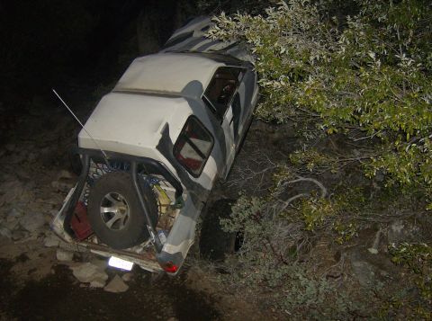 1986 Ford Bronco - This off-road vehicle, likely from the 1980s, is heavily damaged and partially off a dirt path.