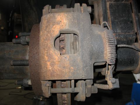 1995 Ford C-350 (Centurion Conversions) - Close-up view of a heavily rusted disc brake caliper and rotor assembly, indicating a need for maintenance.