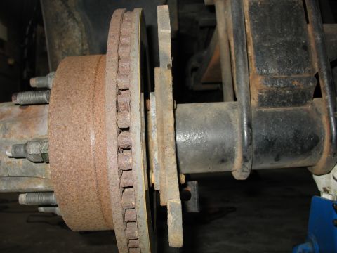 1995 Ford C-350 (Centurion Conversions) - Close-up of a rusty brake rotor, hub, and suspension leaf spring assembly.