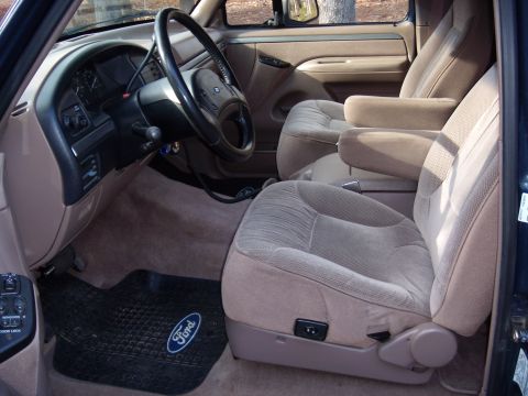 1992 Ford Bronco - The interior of a Ford truck features cloth seats, a tan dashboard, and a black steering wheel with a Ford emblem.