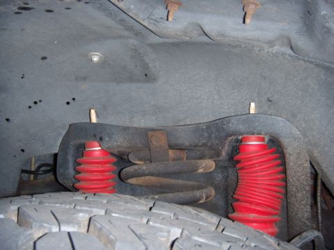 1992 Ford Bronco - Close-up view of the front suspension system, showing red shock absorber boots and a coil spring.