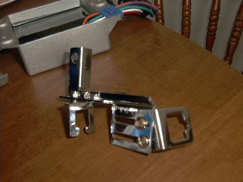 1985 Ford Bronco - A chrome-plated metal bracket or hinge assembly with mounting holes and bolts sits on a wood table, with a gray metal electrical box and co…