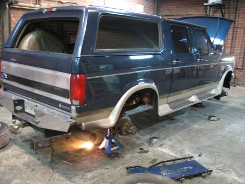 1995 Ford C-350 (Centurion Conversions) - This Ford Bronco is undergoing maintenance, with its wheels off and hood open in a workshop setting.