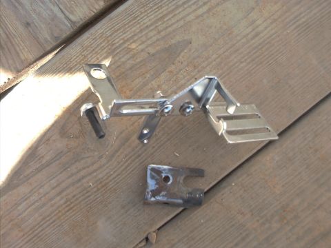 1985 Ford Bronco - Close-up of a polished chrome/stainless steel bracket assembly with mounting holes, Torx screws, and a small bolt, resting on weathered gra…