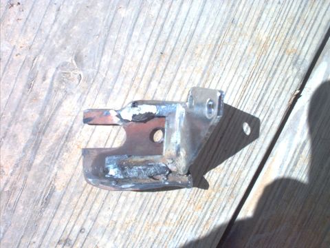 1985 Ford Bronco - A small fabricated steel bracket with fresh weld beads joining a flat tab to a bent U-shaped base, drilled with two bolt holes and a smalle…