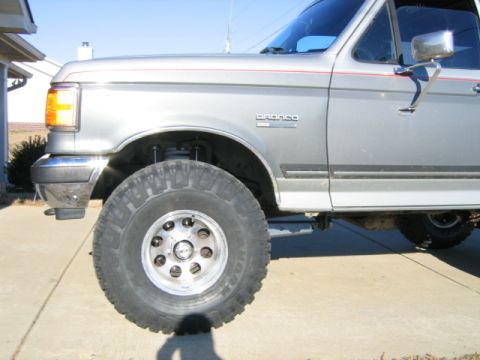 1989 Ford Bronco - Close-up of a silver Ford Bronco's front fender, wheel, and suspension system.