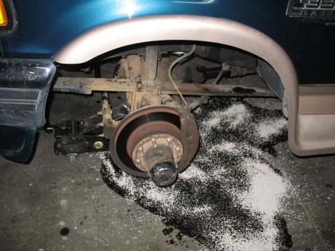 1995 Ford C-350 (Centurion Conversions) - A close-up view of a truck's brake assembly, with a white granular substance scattered on the floor.