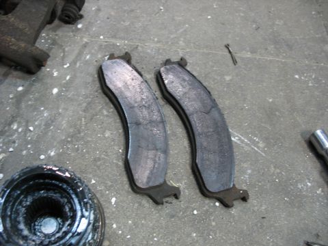 1995 Ford C-350 (Centurion Conversions) - Close-up of two used brake pads and a part of a hub assembly on a concrete surface.