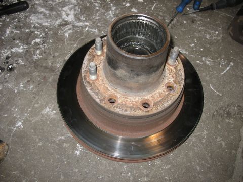 1995 Ford C-350 (Centurion Conversions) - A disassembled brake rotor and hub assembly sits on a concrete surface, showing signs of wear and rust.