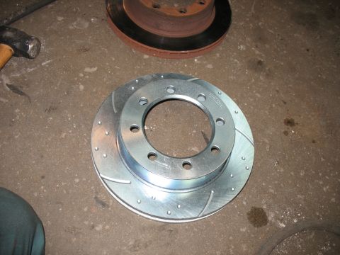 1995 Ford C-350 (Centurion Conversions) - A new brake rotor sits on the floor next to a used, rusty one, with a hammer nearby.