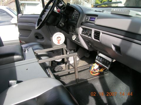 1996 Ford Bronco - The interior of a vehicle shows a custom metal frame installed between the seats, with the dashboard and controls visible.