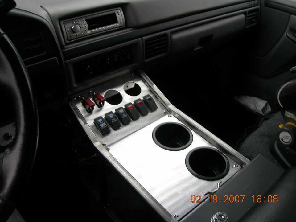 Custom brushed-aluminum center console with switches, gauges and dual cup holders in dark truck interior