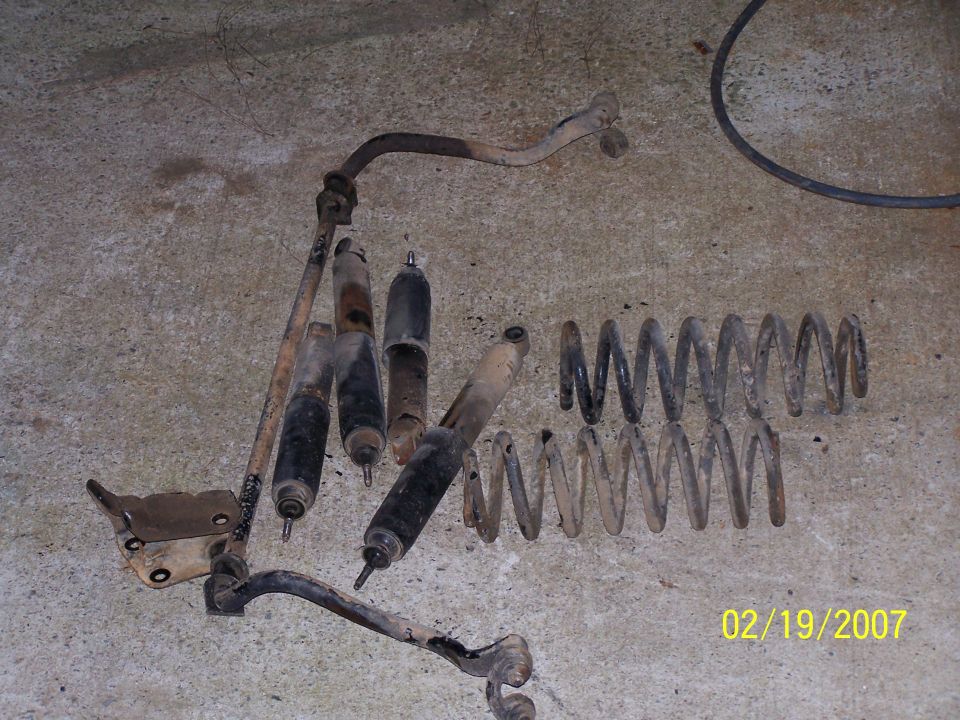 Assorted used suspension components including shock absorbers and coil springs on a concrete floor