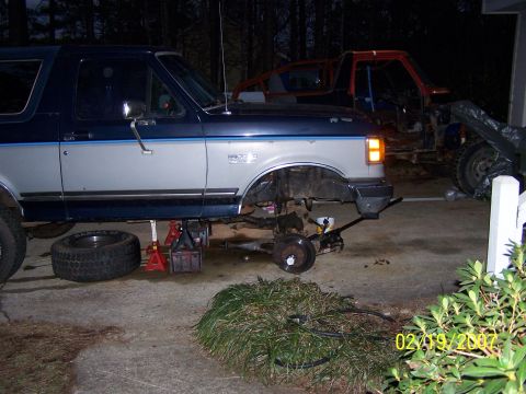 1979 Ford F-150 - A blue and silver Ford Bronco is raised on jack stands, undergoing repairs, with another vehicle visible behind it.