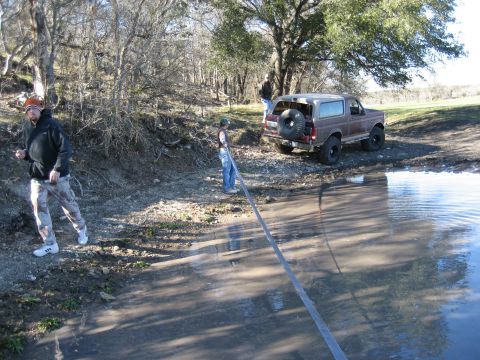 1996 Ford Bronco - A man pulls a hose near a Ford Bronco parked by a muddy area and a large puddle.
