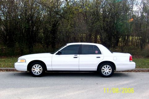 2003 Ford Crown Victoria - A white 2003 Ford Crown Victoria sedan is seen from the side, parked near trees.