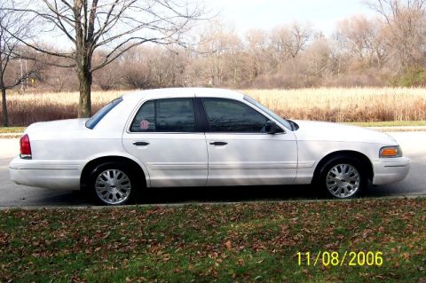 2003 Ford Crown Victoria - This 2003 Ford Crown Victoria is seen from the side, parked on a street with dry grass and trees in the background.
