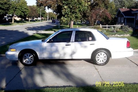 2003 Ford Crown Victoria - A white 2003 Ford Crown Victoria is parked on a concrete driveway with a suburban street in the background.