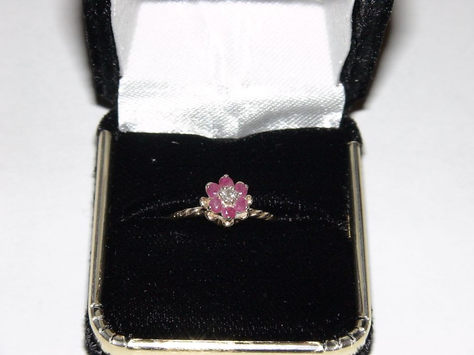 Flower-shaped ring with pink stones and a diamond center in a black velvet box