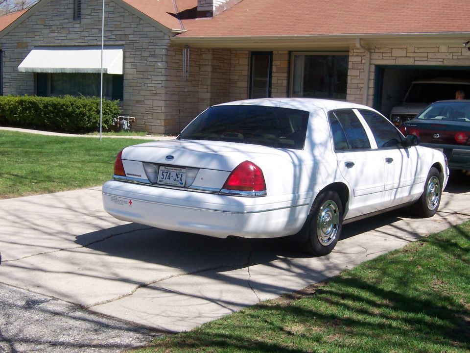 White 2003 Ford Crown Victoria parked in driveway, another car visible in garage