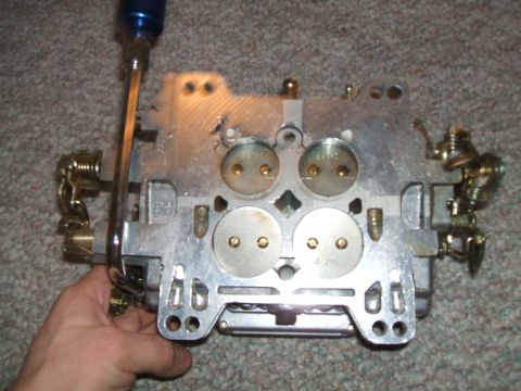 1974 Dodge Challenger - Close-up of a carburetor, possibly for a classic car, with a screwdriver adjusting a linkage.