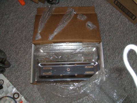 1974 Dodge Challenger - A chrome license plate frame is shown packaged in bubble wrap and a box, with other car parts visible.