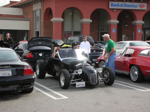 1998 Ford Crown Victoria - black T-bucket-style hot rod roadster sits among classic cars in a parking lot in front of a Bank of America branch.