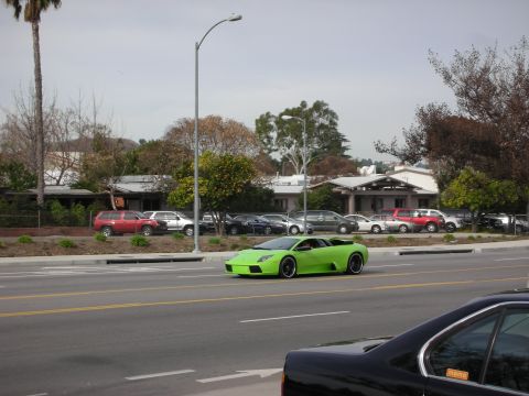 1998 Ford Crown Victoria - bright lime-green Lamborghini drives along a road with a parking lot and houses in the background.