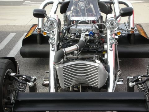 1998 Ford Crown Victoria - Front detail of a custom three-wheeler showing its exposed engine, intercooler, twin round headlights and chrome roll bars.