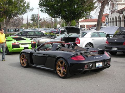 1998 Ford Crown Victoria - black Porsche Carrera GT with bronze wheels is parked at a car show, a green Lamborghini visible nearby.