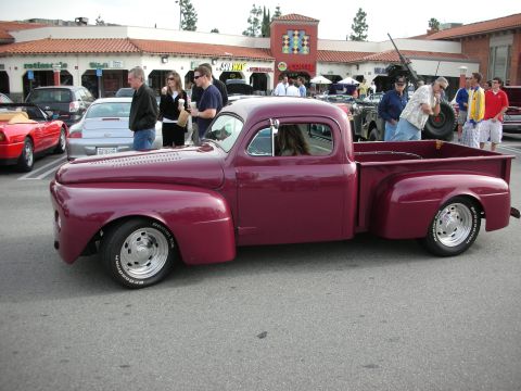 1998 Ford Crown Victoria - maroon customized vintage pickup truck sits at a car-show lot in front of a row of storefronts with onlookers.