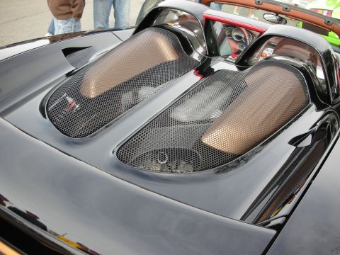 1998 Ford Crown Victoria - Close-up of the carbon-fiber rear engine cover and mesh-grilled air intakes on a black mid-engine sports car.