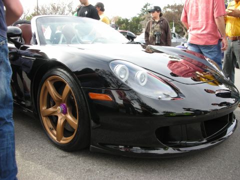 1998 Ford Crown Victoria - Front three-quarter close-up of a black Porsche Carrera GT showing its headlight, bronze wheel and air intake at a crowded show.
