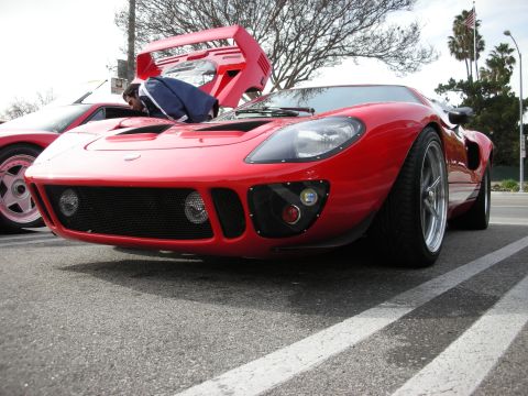 1998 Ford Crown Victoria - red GT40-style mid-engine coupe with its clamshell hood raised sits at a car show on a sunny day.