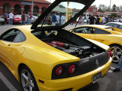 1998 Ford Crown Victoria - yellow Ferrari coupe sits with its rear engine lid raised in a parking lot car show, crowd and other sports cars behind it.