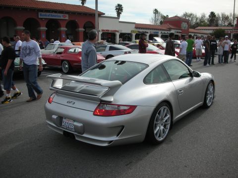 1998 Ford Crown Victoria - silver Porsche 911 GT3 with rear wing is parked among classic and sports cars at a busy parking-lot car show.